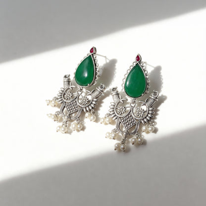 Ornate earrings with green teardrop stones and pearl-like elements on a white background