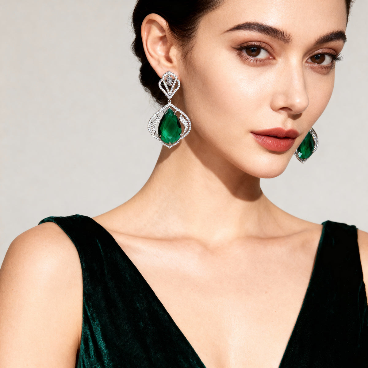 Woman wearing emerald green earrings with a neutral background