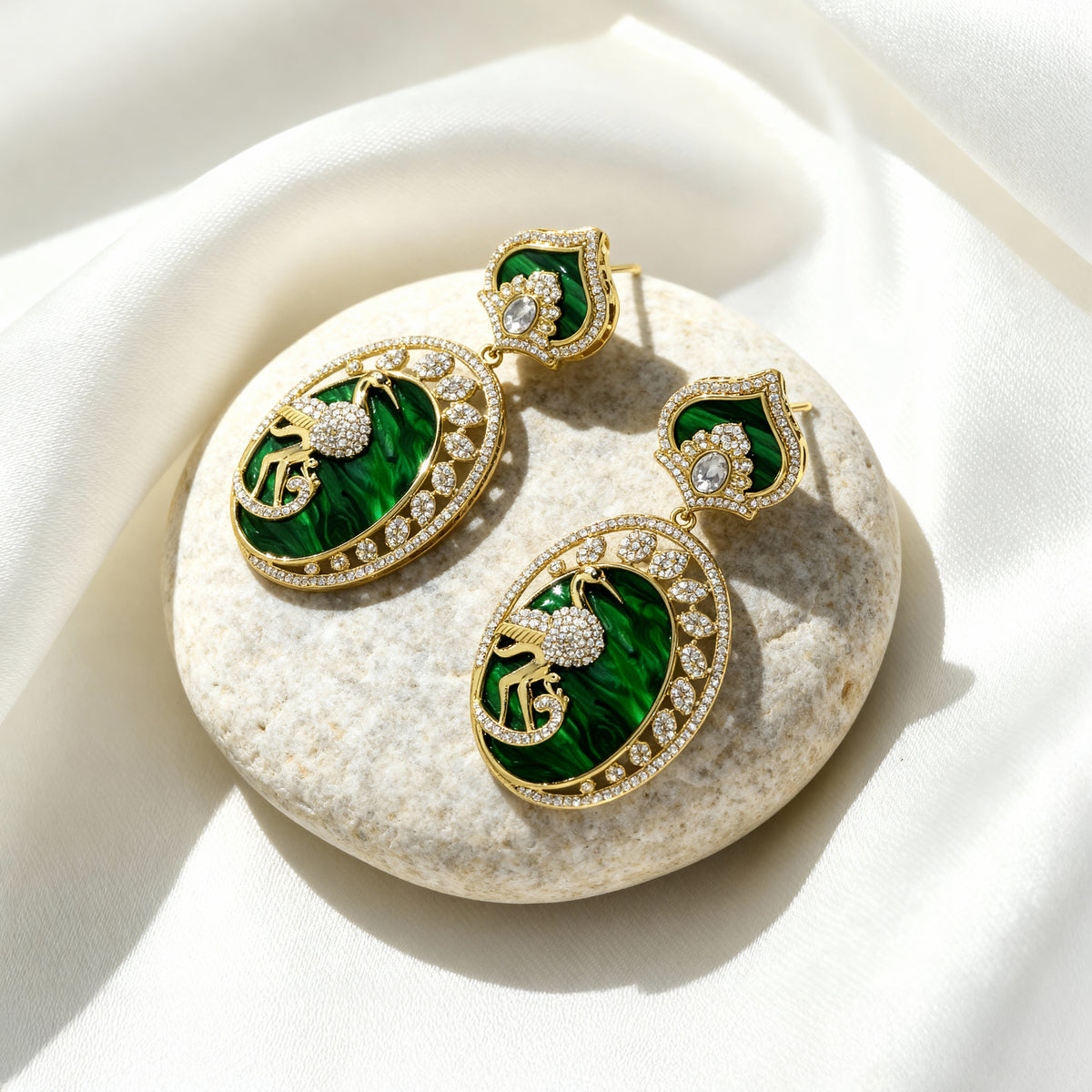 Pair of green and gold earrings on a white stone
