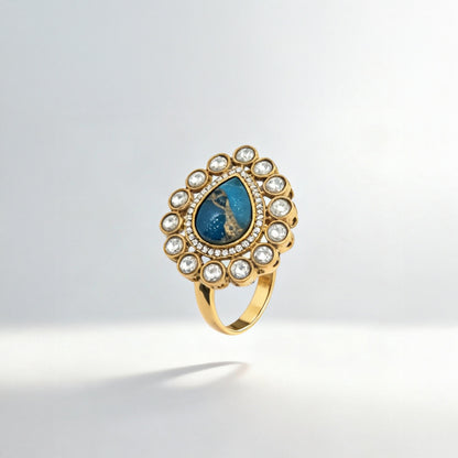Gold ring with a blue gemstone and pearl accents on a light gray background