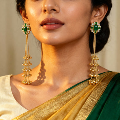 Woman wearing gold earrings with green gemstones, dressed in a green and gold saree.