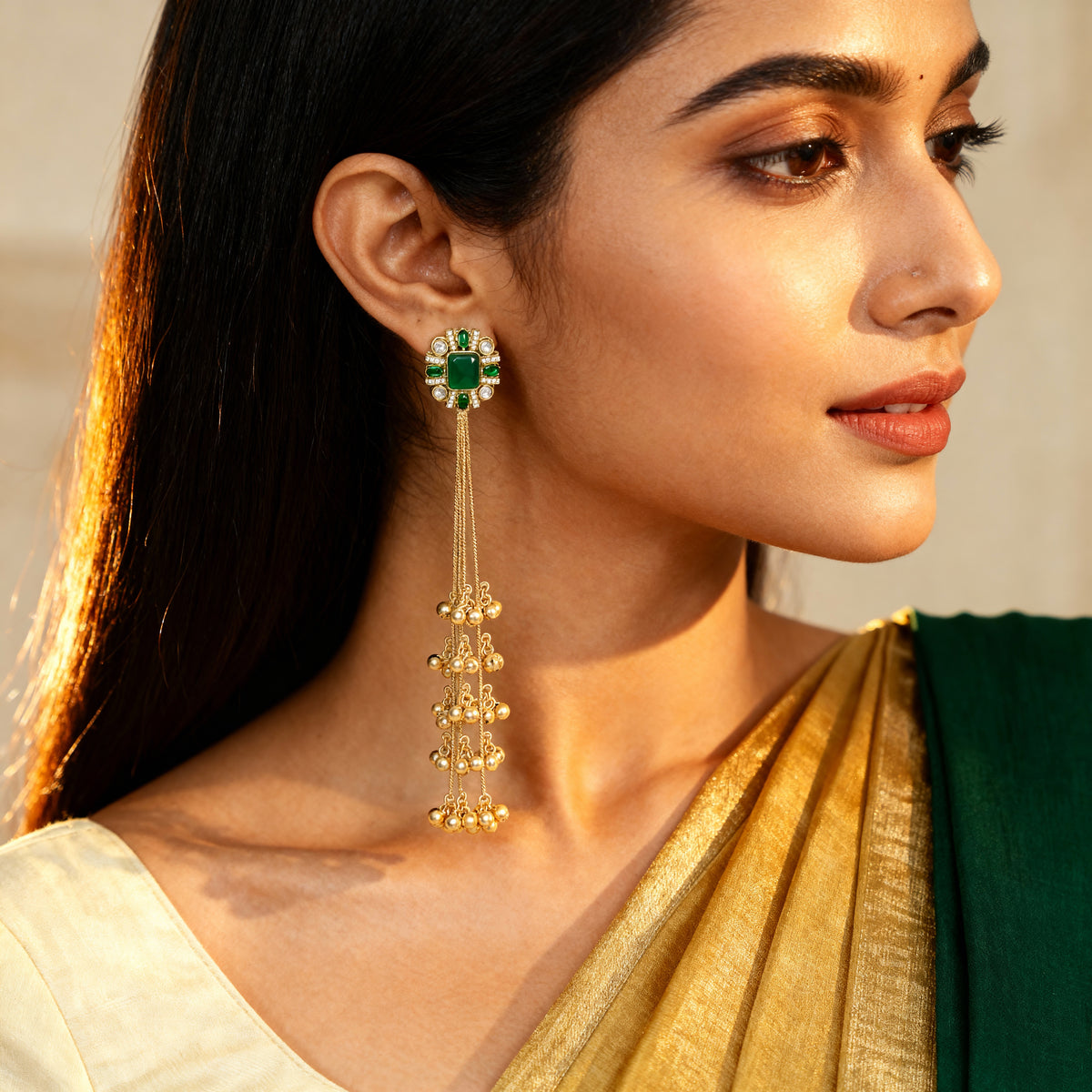 Woman wearing gold earrings with green gemstones, dressed in a green and gold traditional outfit.