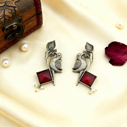 Pair of silver earrings with red stones on a decorative surface with pearls and a wooden box.