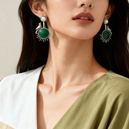 Close-up of a woman wearing green earrings with a neutral background