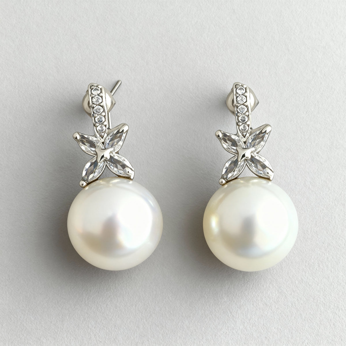 Pearl earrings with silver floral tops on a light gray background