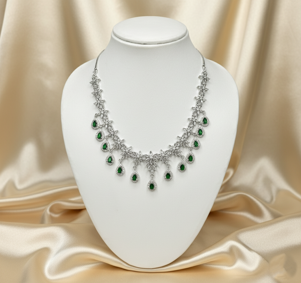 Silver necklace with green gemstones on a white stand against a beige satin background