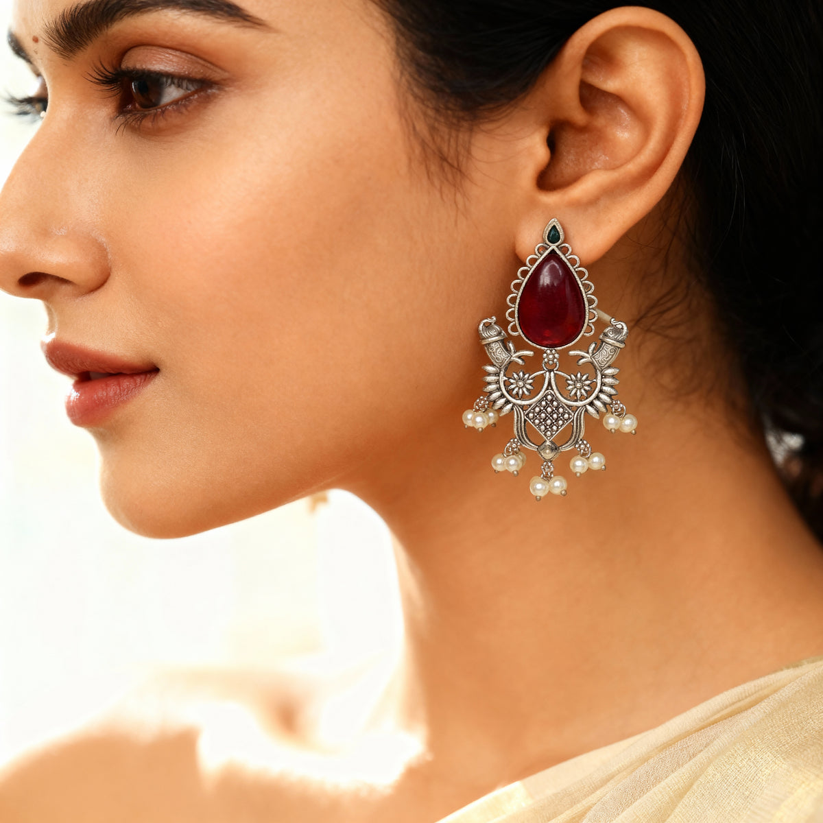 Close-up of a woman wearing an ornate earring with a red gemstone.