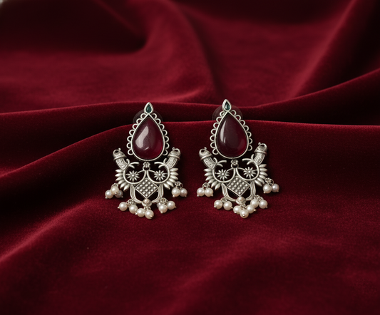 Silver earrings with red stones on a red fabric background