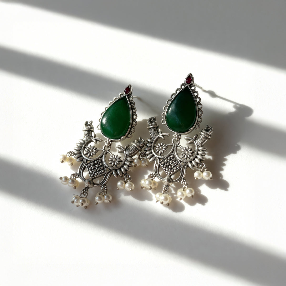 Ornate earrings with green teardrop stones and pearl-like beads on a light background
