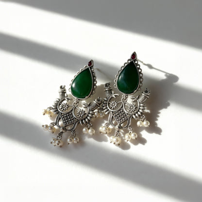 Ornate earrings with green teardrop stones and pearl-like beads on a light background