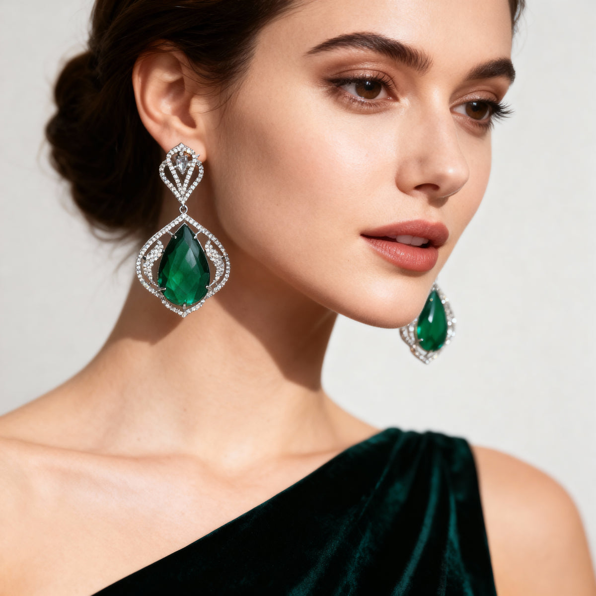 Woman wearing emerald green teardrop earrings with a neutral background