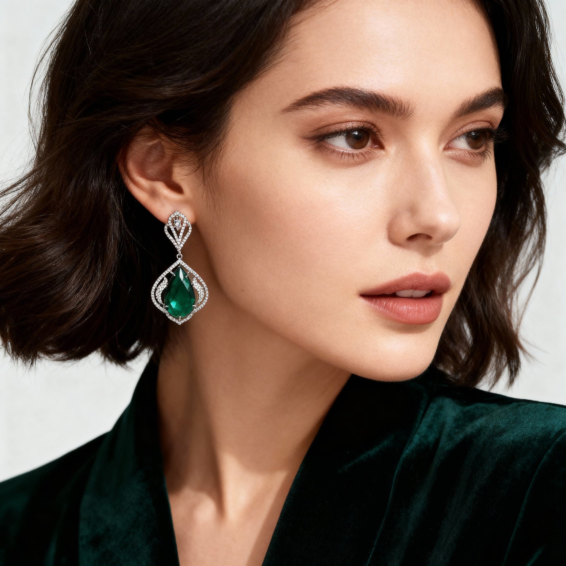 Close-up of a woman wearing emerald green earrings with a white background
