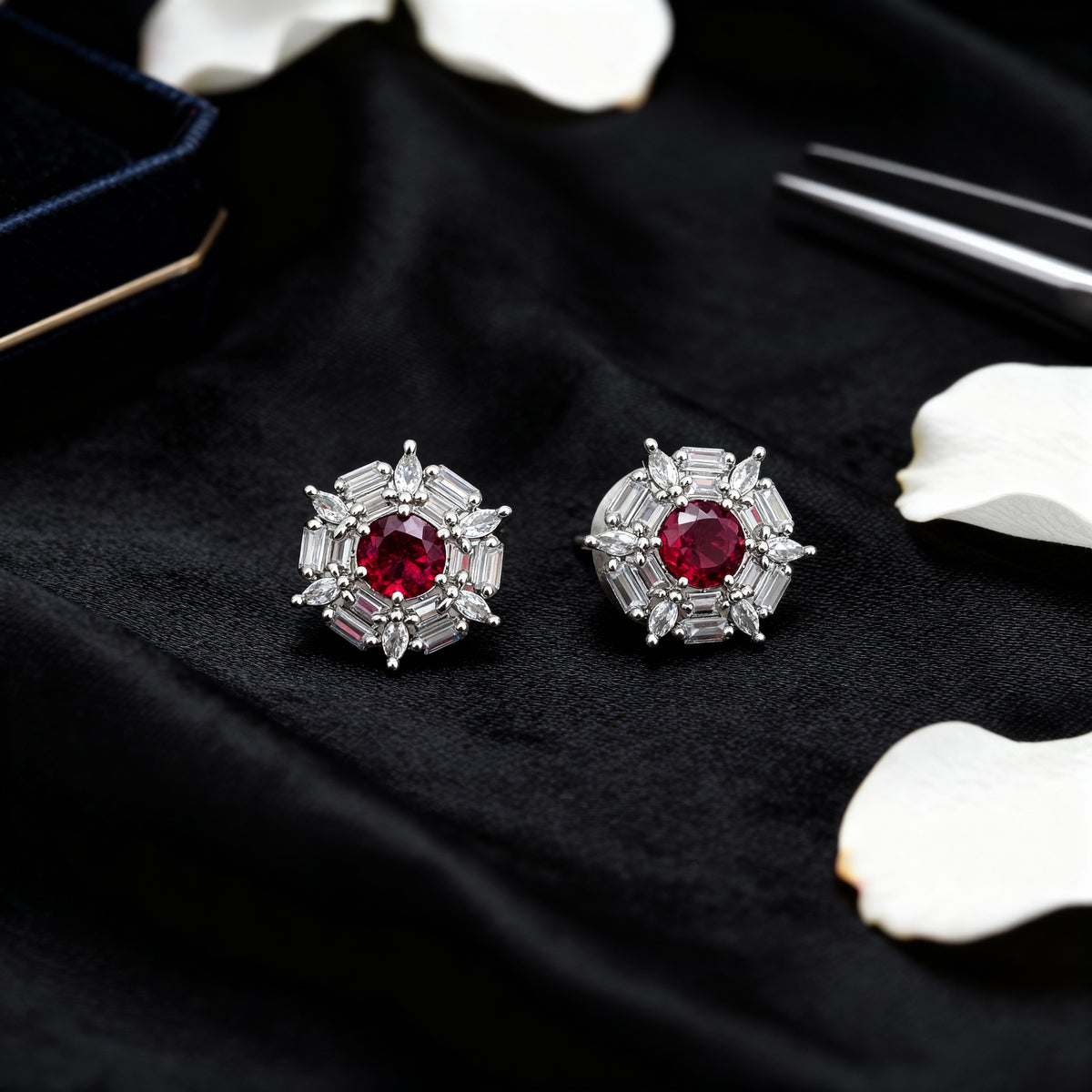 Pair of silver earrings with red gemstones on a black surface with white flowers.