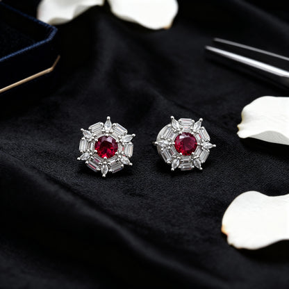 Pair of silver earrings with red gemstones on a black surface with white flowers.