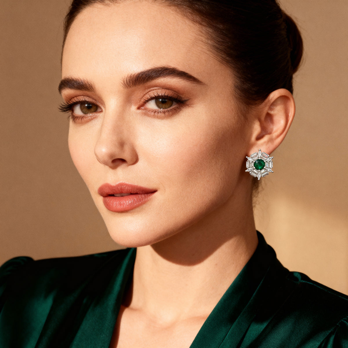 Close-up of a woman wearing emerald green earrings against a beige background